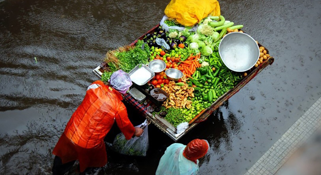 Foto of poeple walking with colourful vegetables on a tow truck through a flooded street